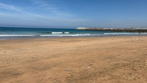 A wide sandy beach with waves approaching the shore, a rocky breakwater in the distance, and scattered birds. - Villa au calme, jardin spacieux et confort moderne (Skhirat)