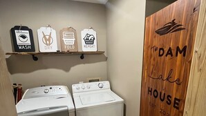 Un lavadero con dos lavadoras, un tendedero y una puerta de madera con la inscripción 'The DAM Lake House'.