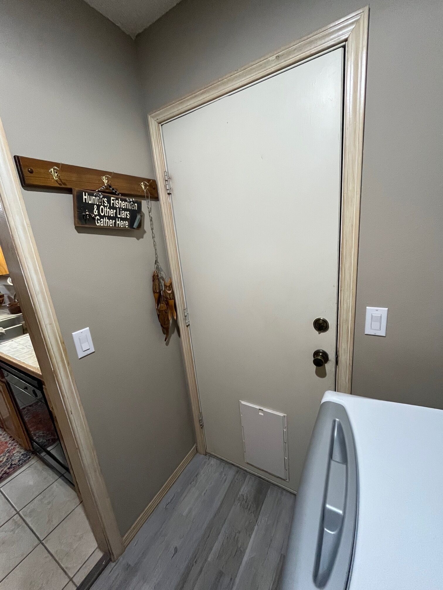 Una habitació amb la porta tancada, un senyal de fusta a dalt i un aparell blanc al primer pla.