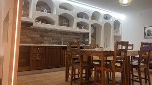 Una cuina amb salabost a la paret, armaris de fusta i zona de menjador amb taula i cadires.