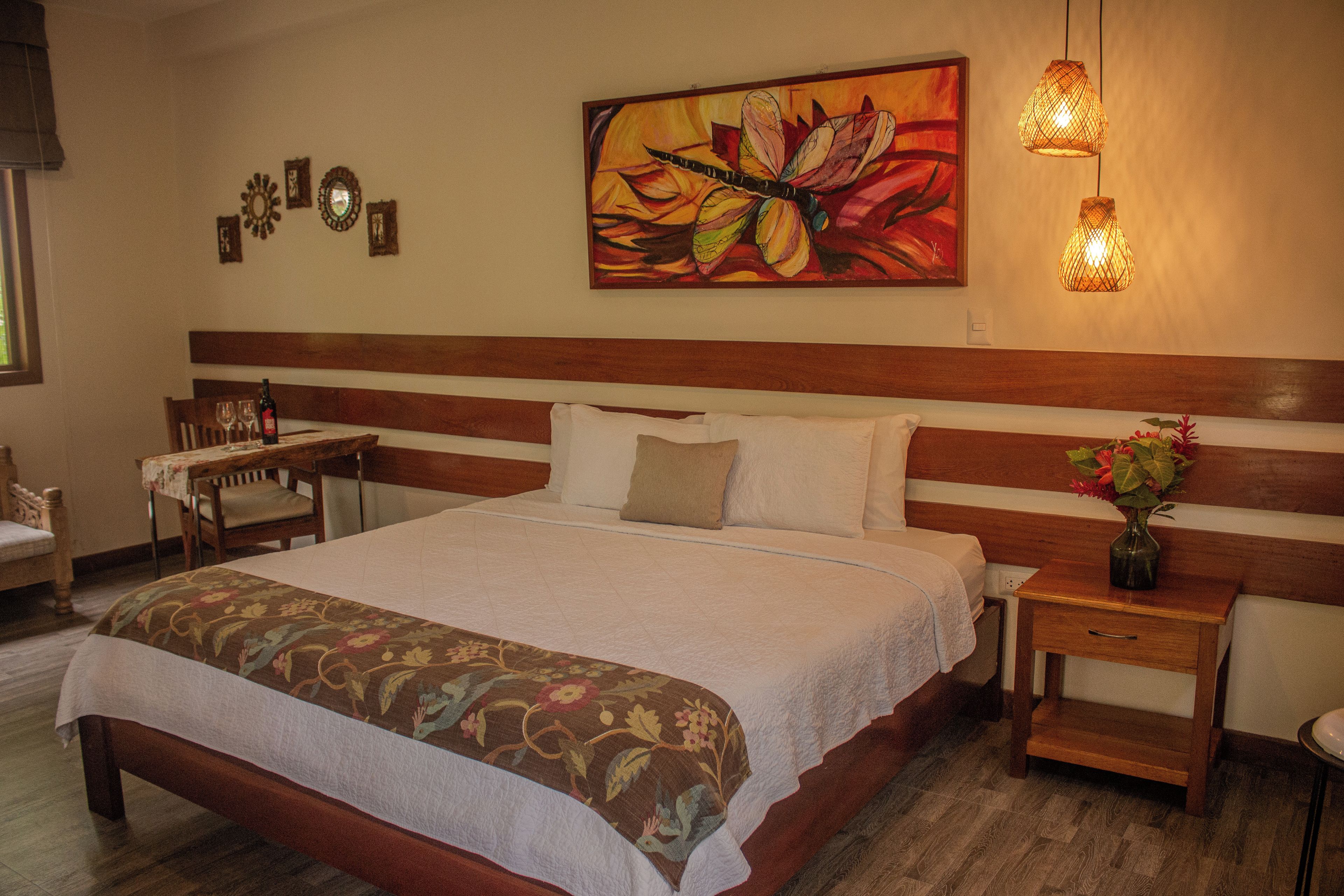Quarto de hotel com cama grande, mesa de cabeceira, cadeira, mesa e um quadro na parede.