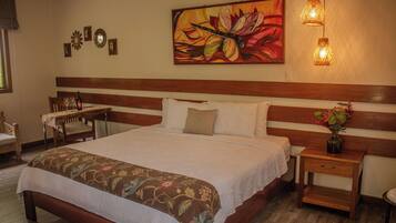 Quarto de hotel com cama grande, mesa de cabeceira, cadeira, mesa e um quadro na parede.