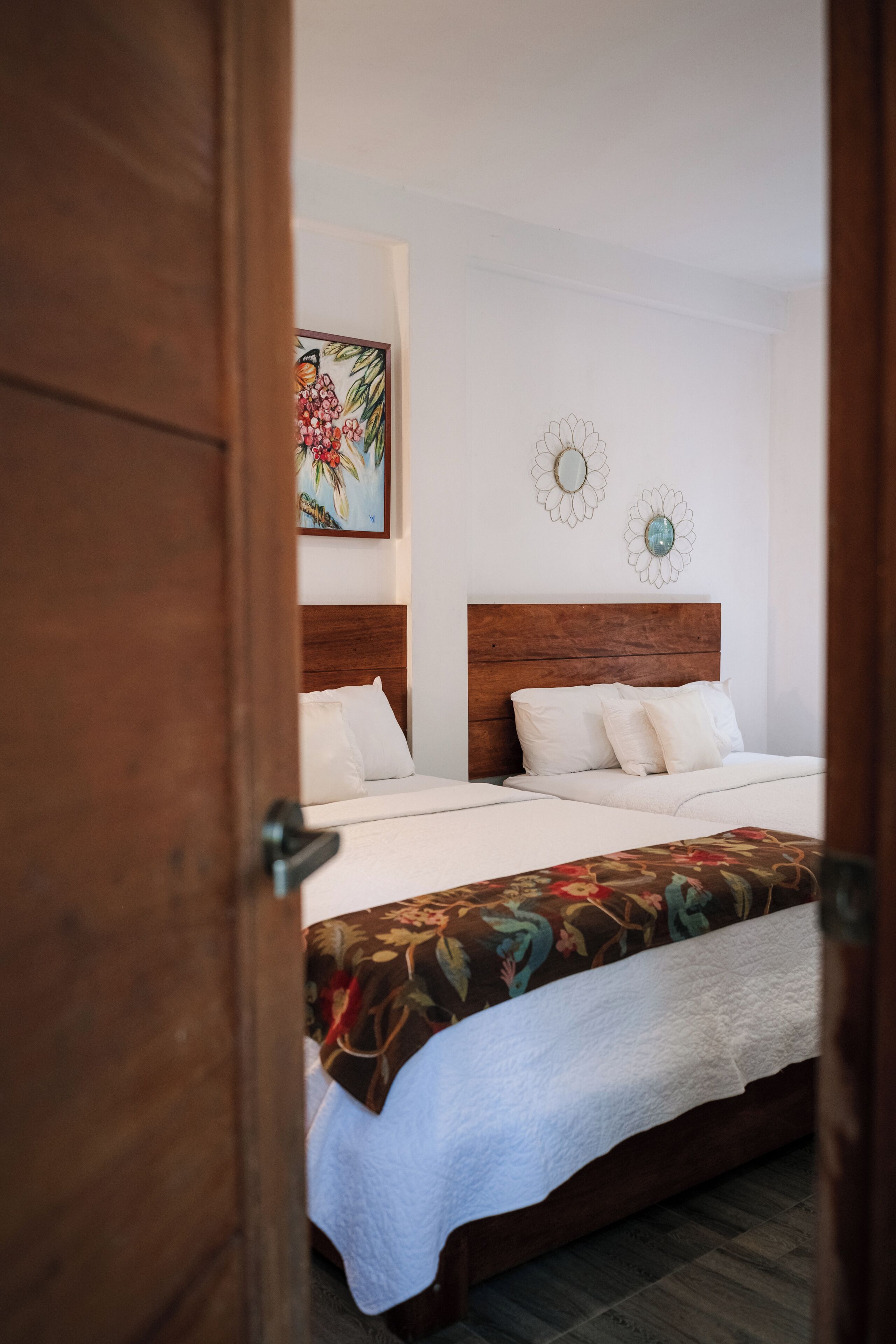 A bedroom with a wooden headboard, white bedding, and a floral-patterned bedspread.