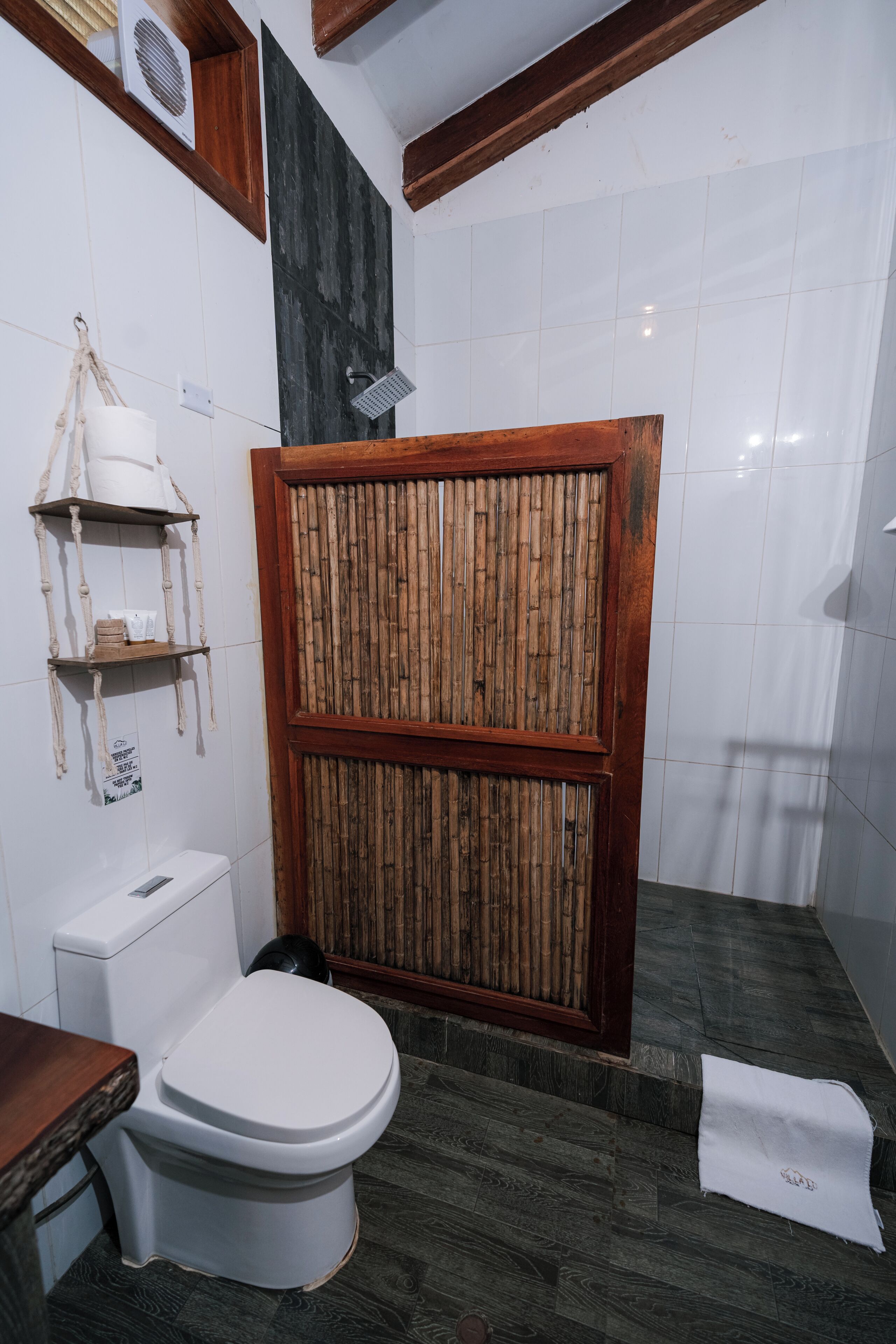 Un baño con inodoro, cabina de ducha de madera y estante de bambú.