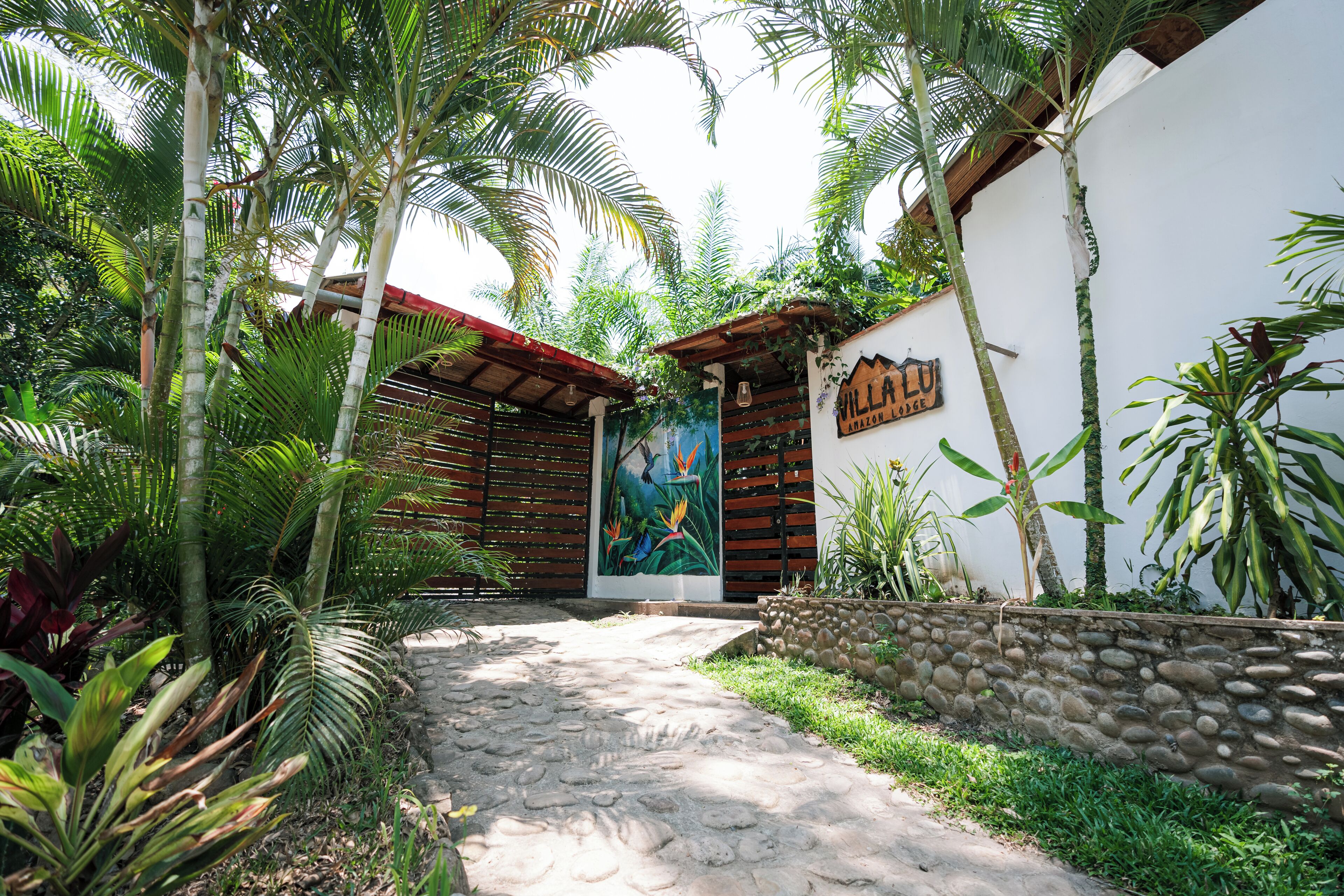 A pathway leading to a building with a mural, surrounded by lush tropical plants.