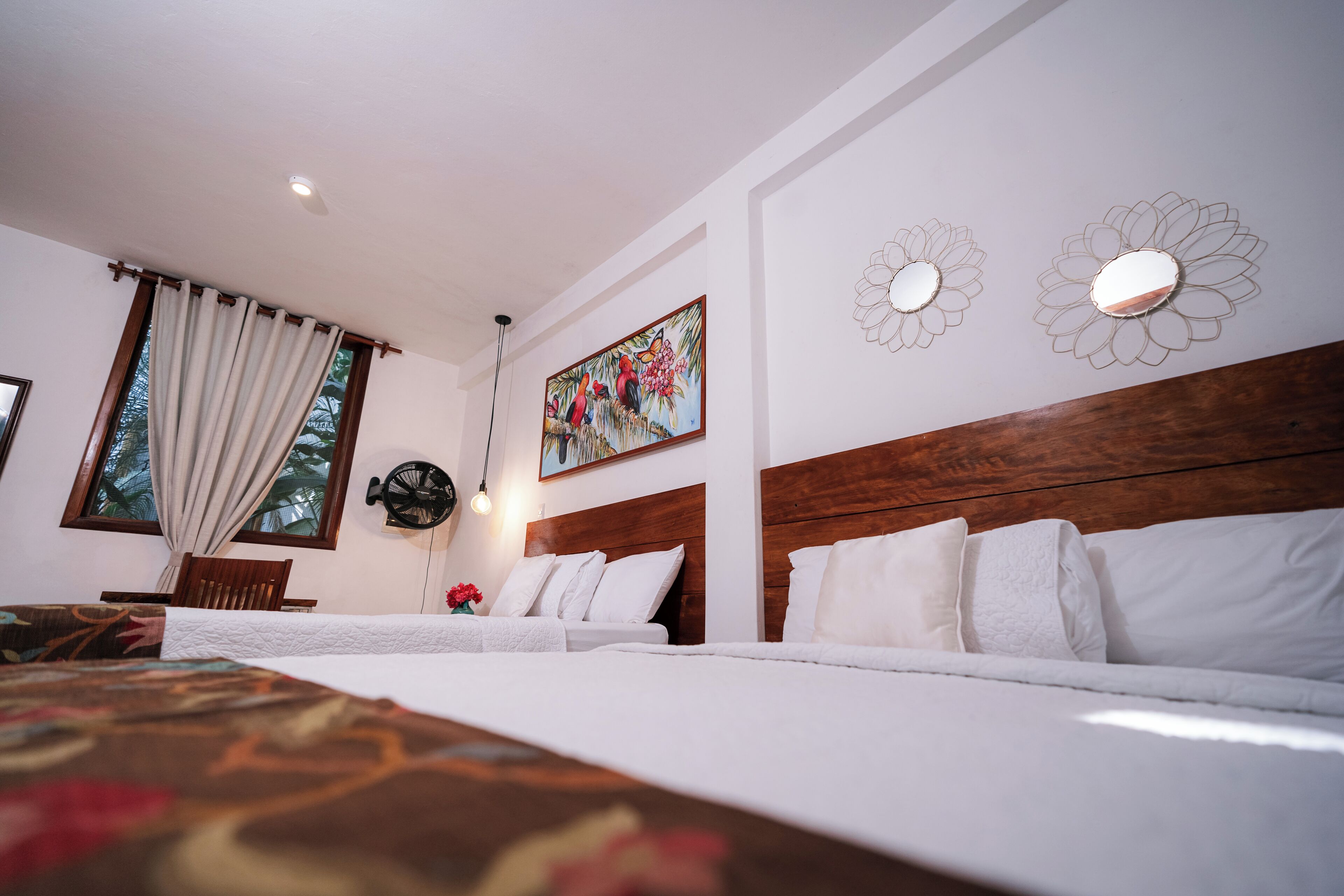 Une chambre d’hôtel avec deux lits, une tête de lit en bois, un tableau et une fenêtre avec des rideaux.