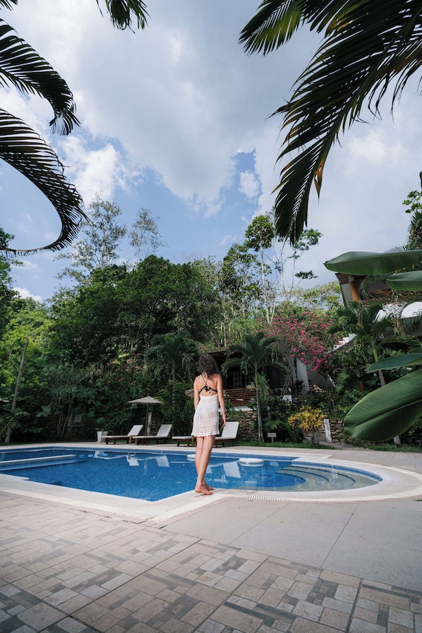 A pool area with a person standing by the pool, surrounded by lush greenery and a clear sky. - Villa Lu Amazon Lodge (Tarapoto)