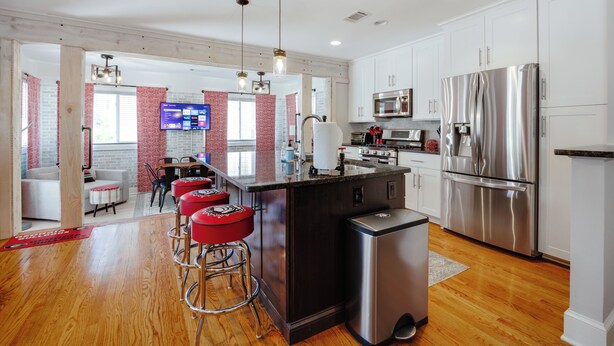 A modern kitchen with stainless steel appliances, a central island with bar stools, and a dining area with a TV.