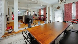 A spacious dining area with a wooden table and chairs, a kitchen in the background, and a red and white patterned wall.