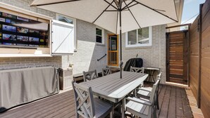 An outdoor patio with a table and chairs, a large umbrella, and a TV mounted on the wall.