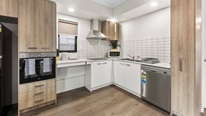 A modern kitchen with white cabinetry, a built-in oven, a microwave, and a dishwasher. - 3BR Home Near Werribee Plaza w/ Free Parking + Free Wifi (Mambourin)