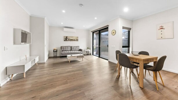 A modern living room with a sofa, coffee table, and dining table with chairs. - 3BR Home Near Werribee Plaza w/ Free Parking + Free Wifi (Mambourin)