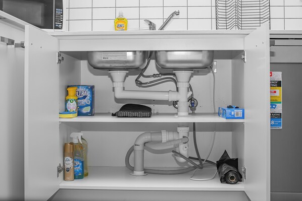 A kitchen with a sink, dishwasher, and various cleaning supplies.