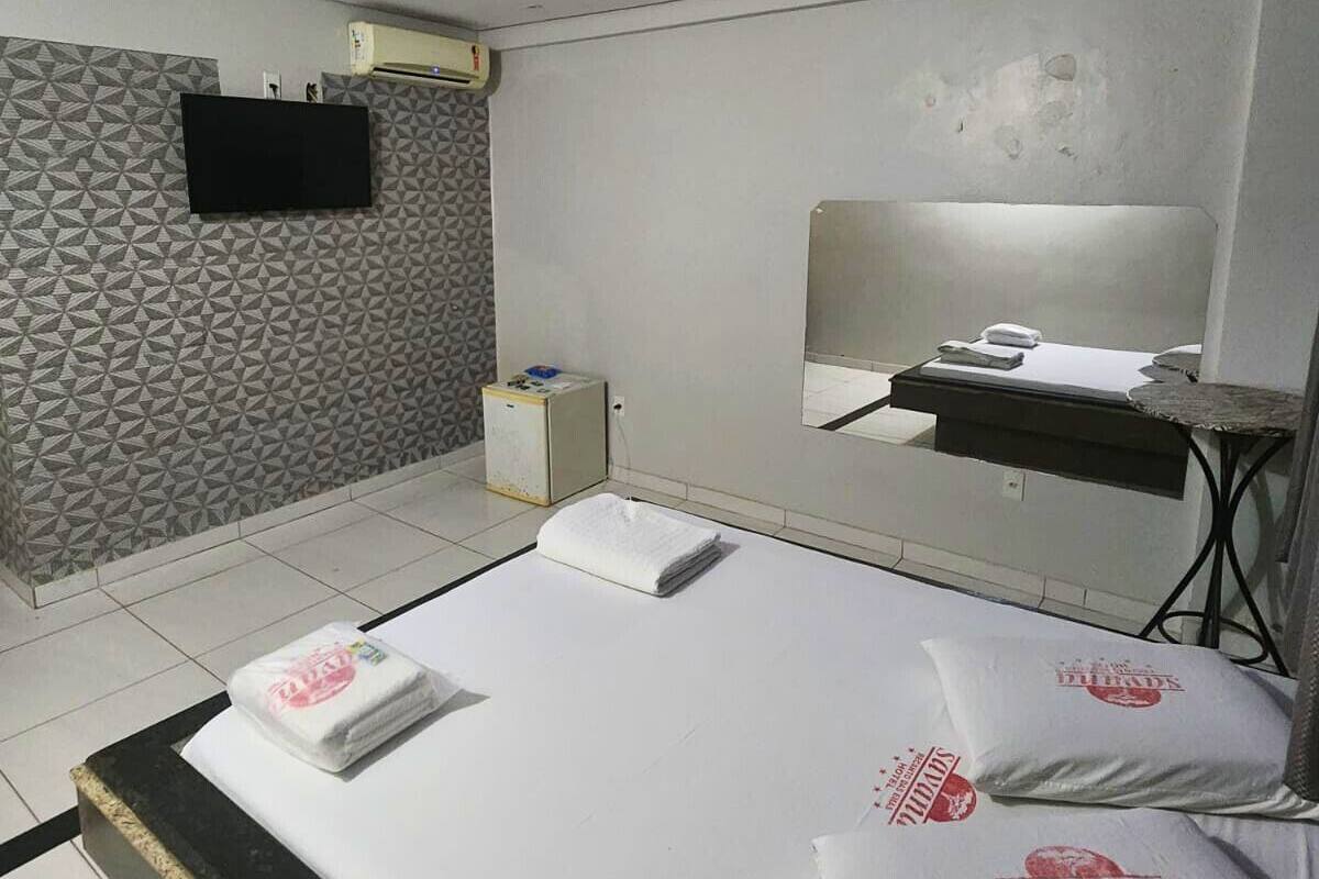 A hotel room with a bed, a flat-screen TV, a mirror, a small table, and a wall-mounted air conditioner.