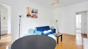A modern living room with a round table, blue sofa, and artwork on the wall. - Charming Flat -2br/6p- Montorgueil (Paris)
