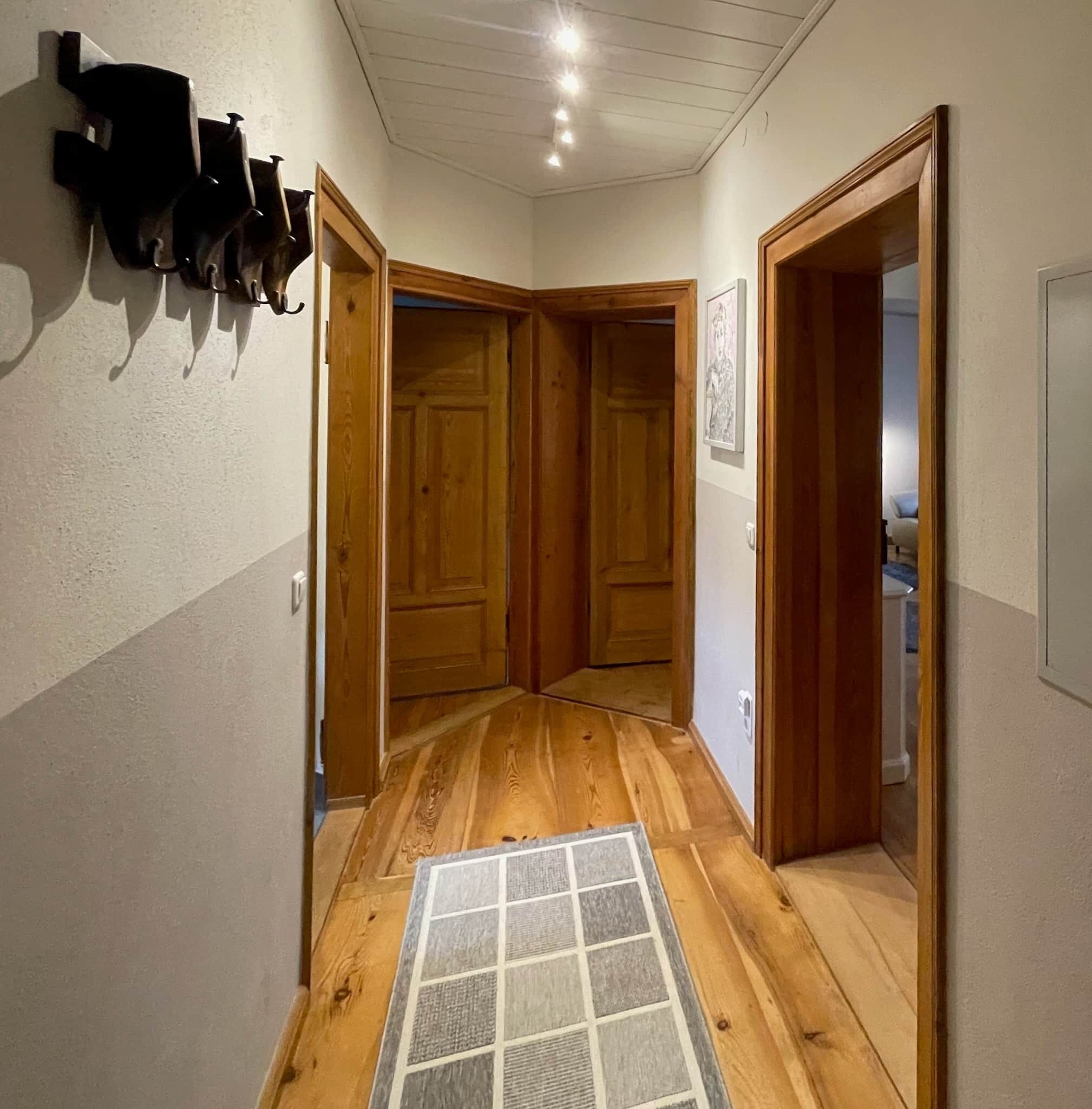 Een hal met houten vloer, een betegelde mat bij de ingang en houten deuren.