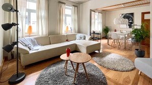 Un salon moderne avec un canapé d’angle, une table basse ronde en bois et un coin repas comprenant une table et des chaises blanches.