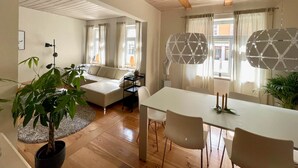 Un salon moderne avec un canapé, une table à manger et des chaises. On y trouve également une plante en pot et une lampe.