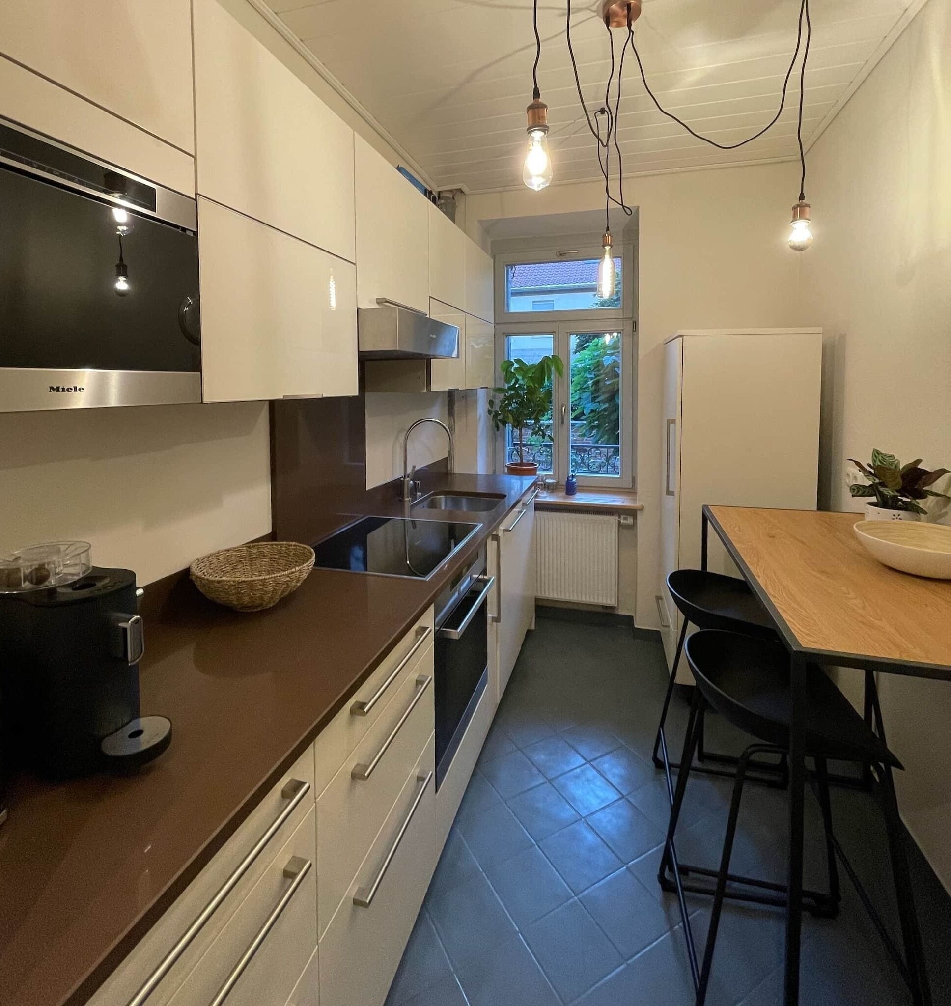 Una cocina moderna con armarios blancos, encimera negra y estufa integrada. Se ve una ventana con vistas a zonas verdes.
