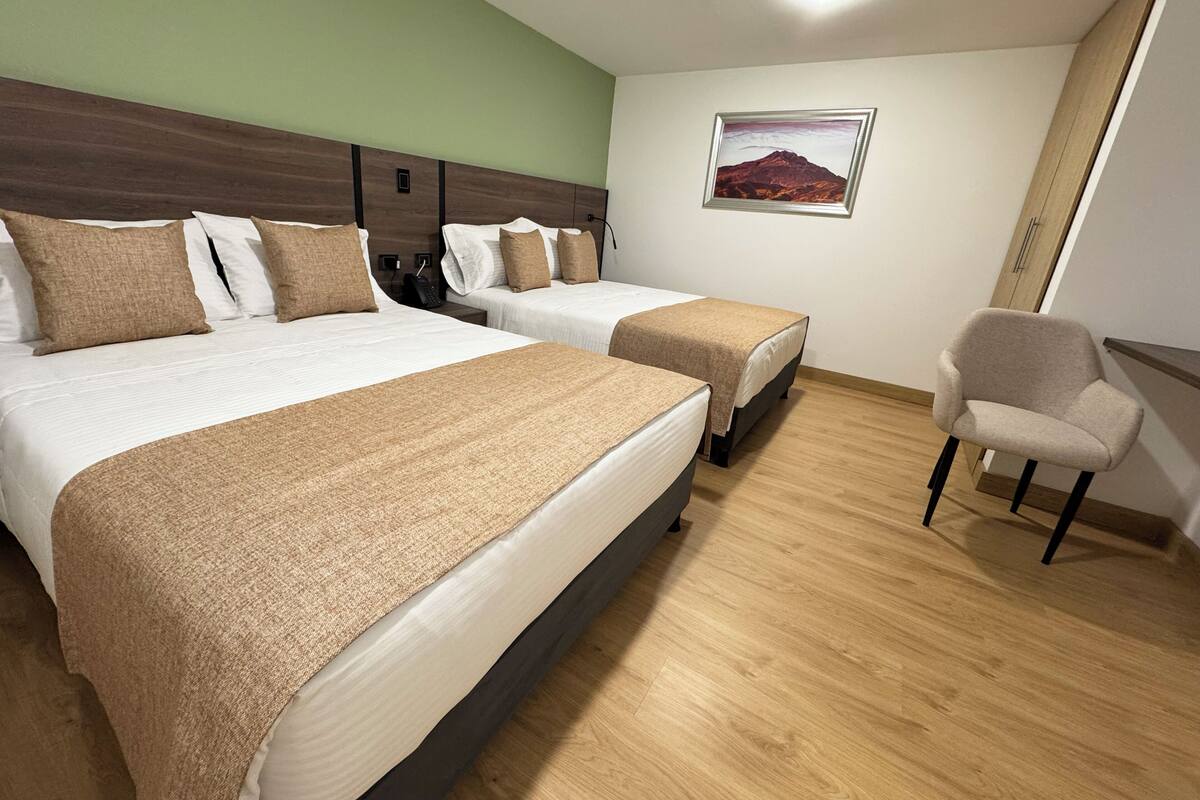 Quarto de hotel com duas camas, uma cadeira e um quadro na parede.