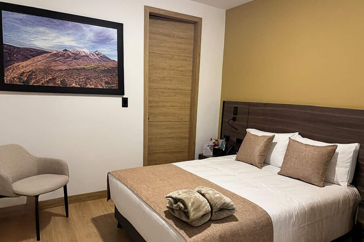 Quarto de hotel com cama, cadeira, porta de madeira e quadro na parede.