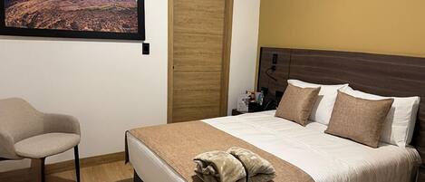Una habitación de hotel con una cama, una silla, una puerta de madera y un cuadro en la pared.