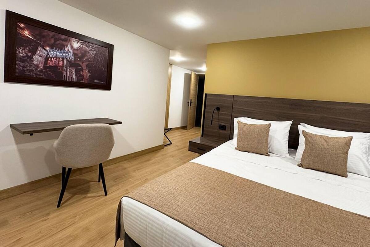 Quarto de hotel com cama, mesa de cabeceira, cadeira e um quadro na parede.