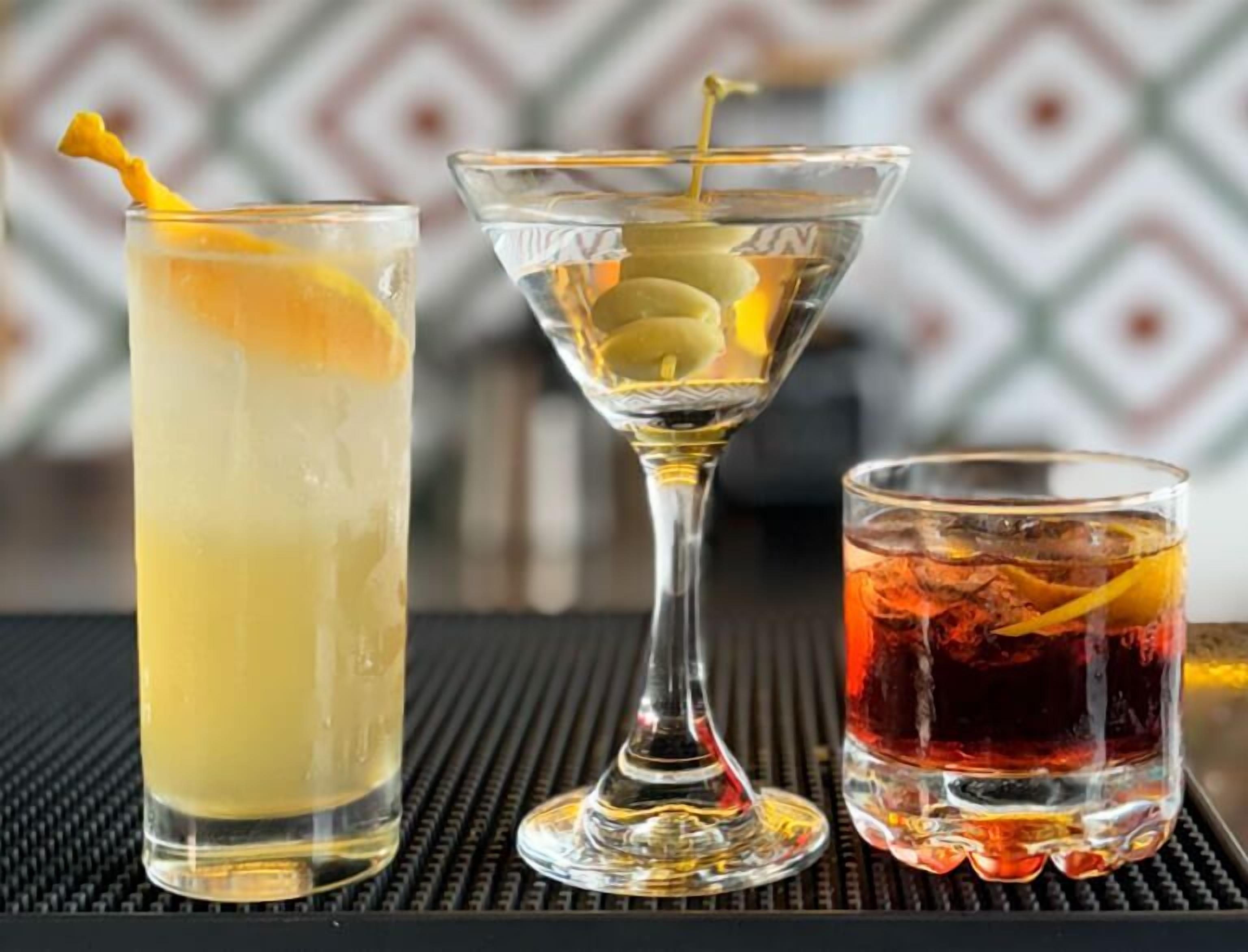 Three different glasses of beverages with lemon slices and a cocktail with a garnish.