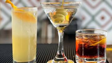 Three different glasses of beverages with lemon slices and a cocktail with a garnish.