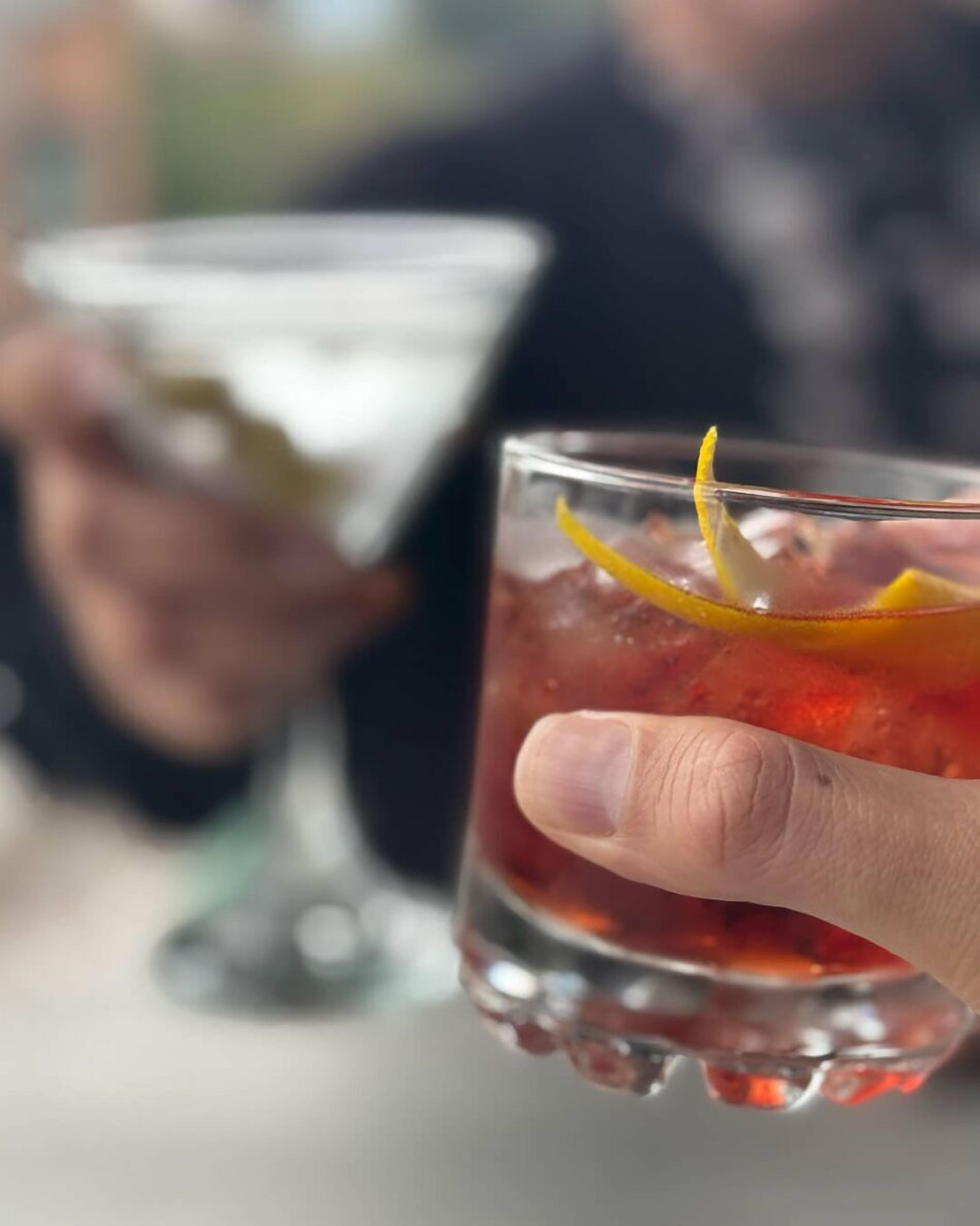A hand holding a cocktail glass with a lemon slice garnish.
