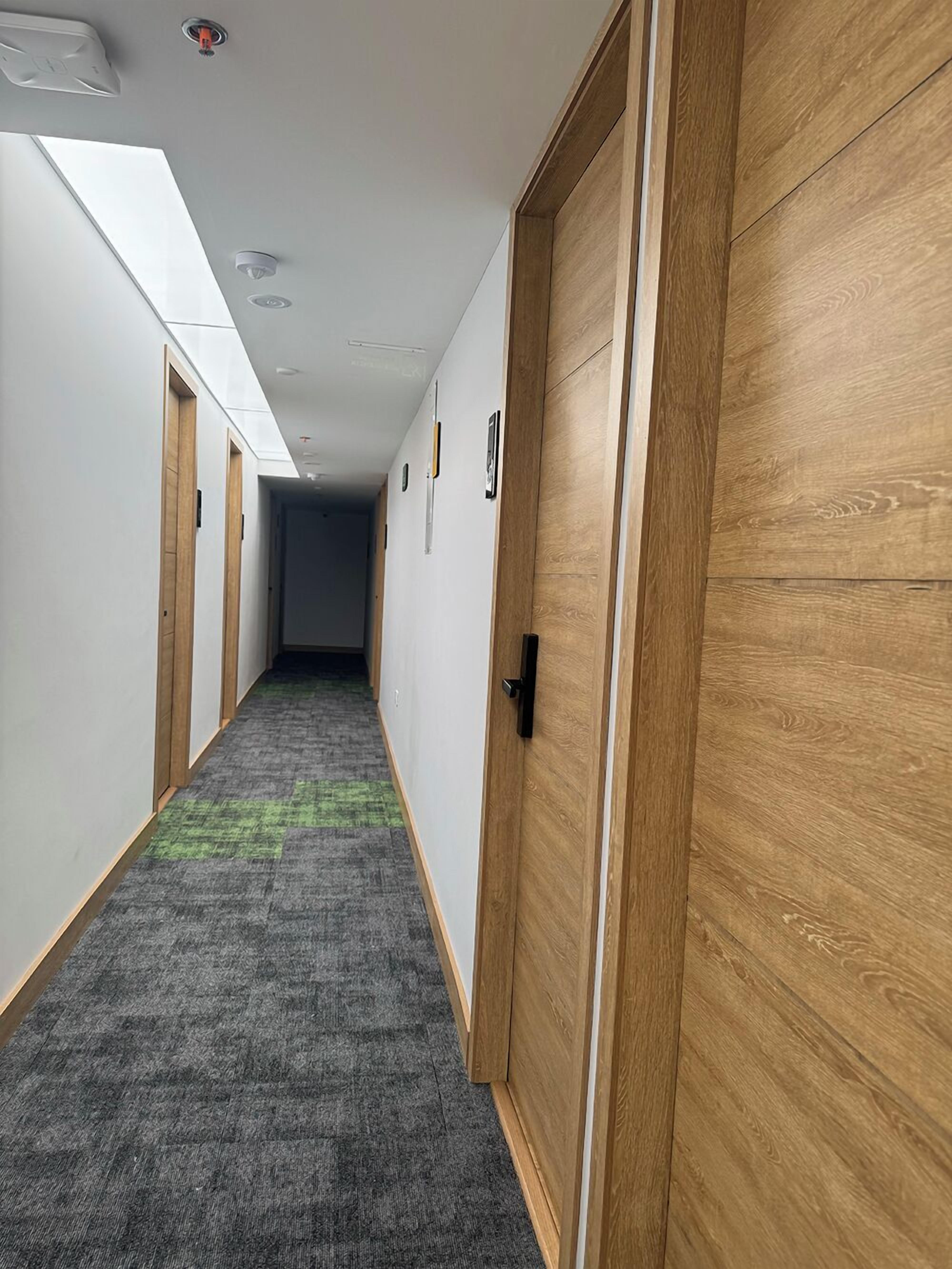 Un pasillo con puertas de madera, alfombra gris y tragaluz.
