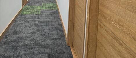 Un pasillo con puertas de madera, alfombra gris y tragaluz.