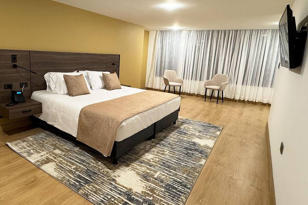 Quarto moderno com cama grande, mesas de cabeceira, escrivaninha e uma cadeira.