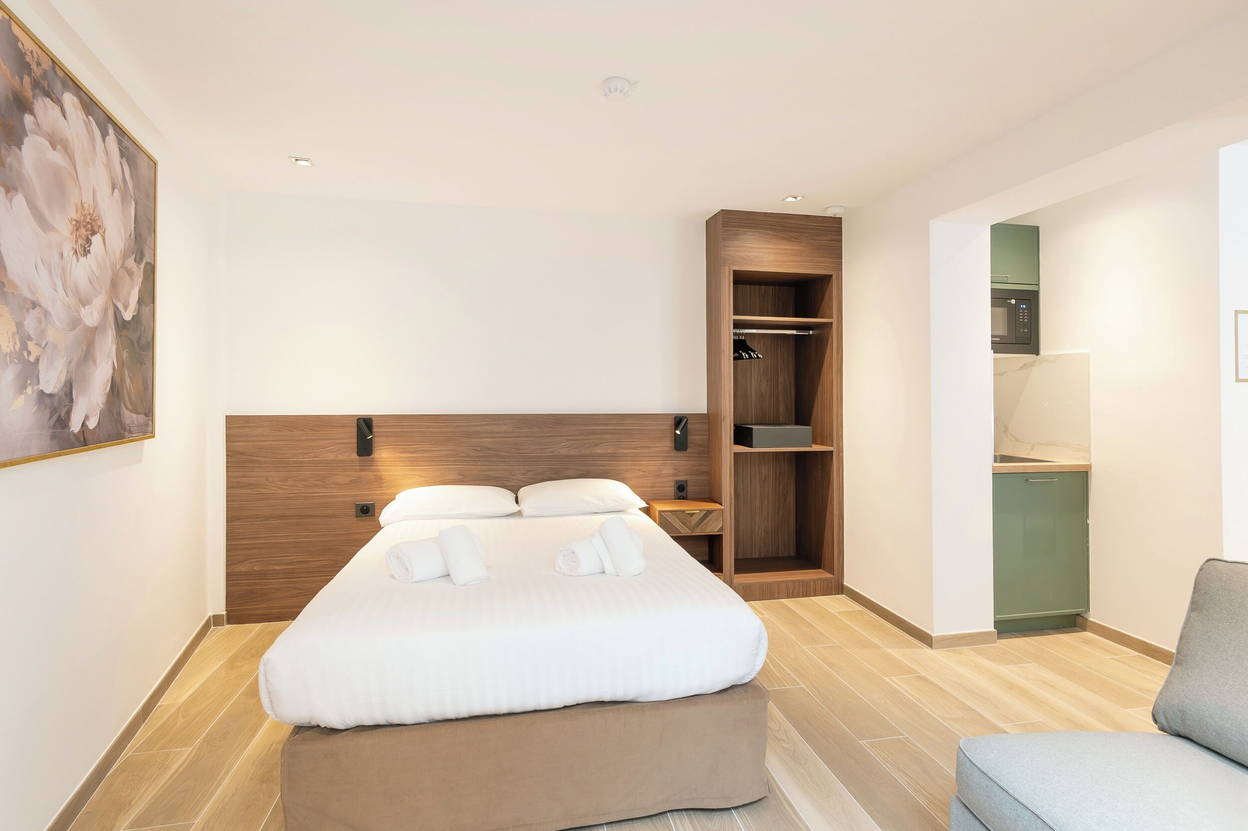 Una habitación de hotel moderna con una cama grande, un cabecero de madera, un armario empotrado y una pequeña kitchenette.