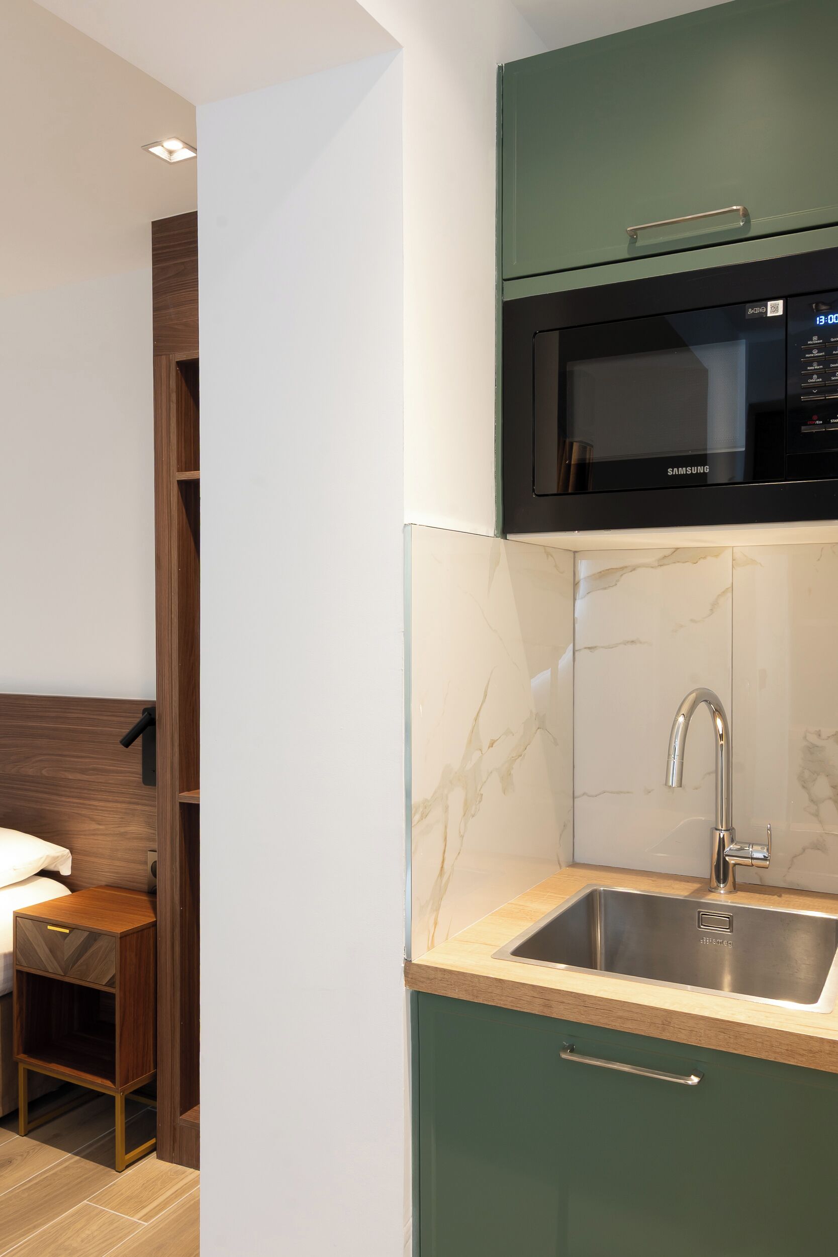 Een kleine keuken met een ingebouwde magnetron, een rvs-spoelbak en een houten kast.