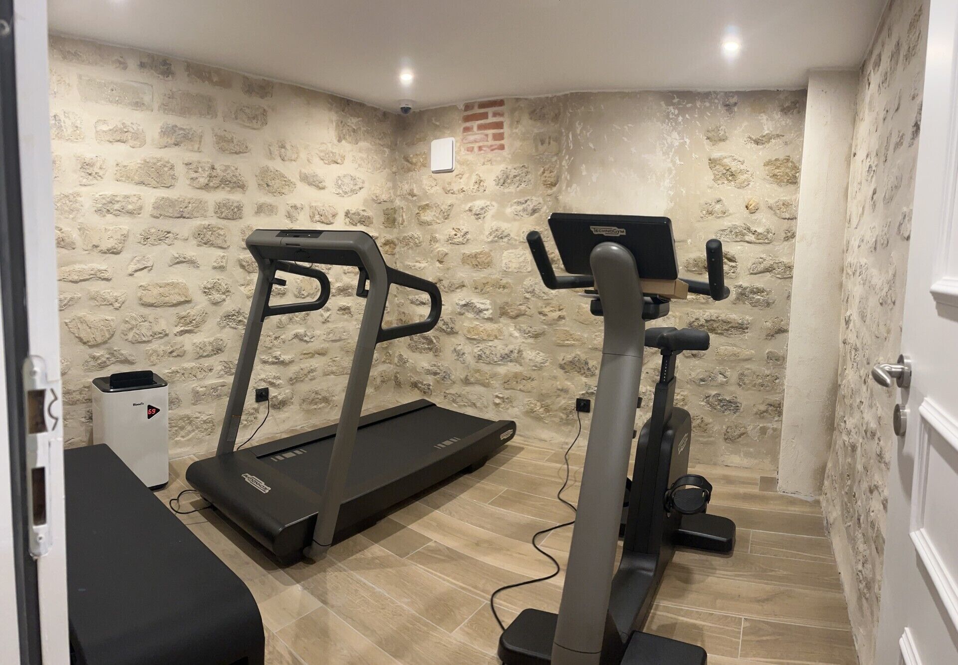 A room with a treadmill and elliptical machine, stone walls, and a small white cabinet.