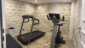 A room with a treadmill and elliptical machine, stone walls, and a small white cabinet.