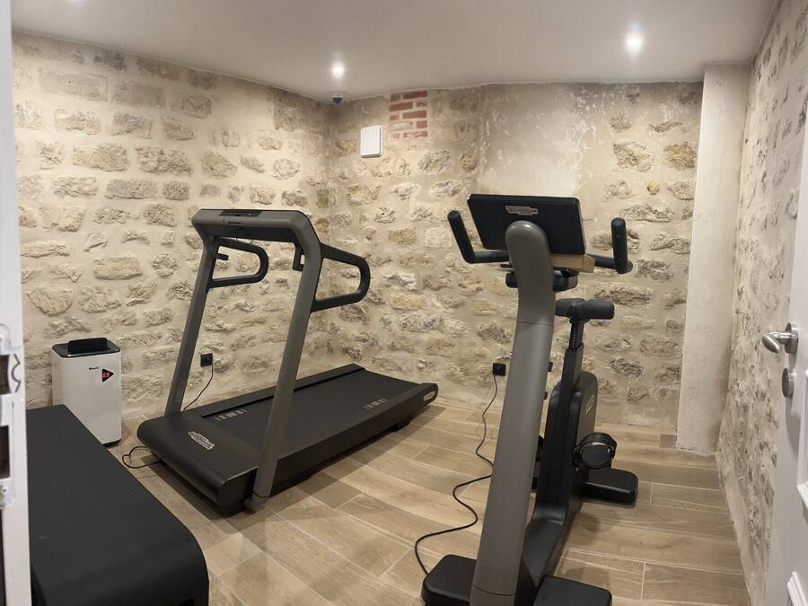 A room with a treadmill and elliptical machine, stone walls, and a small white cabinet.
