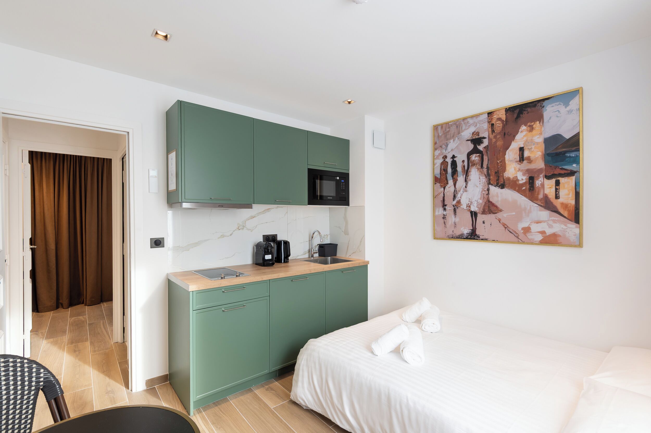 Ett modernt hotellrum med en säng, ett litet pentry och en tavla på väggen.