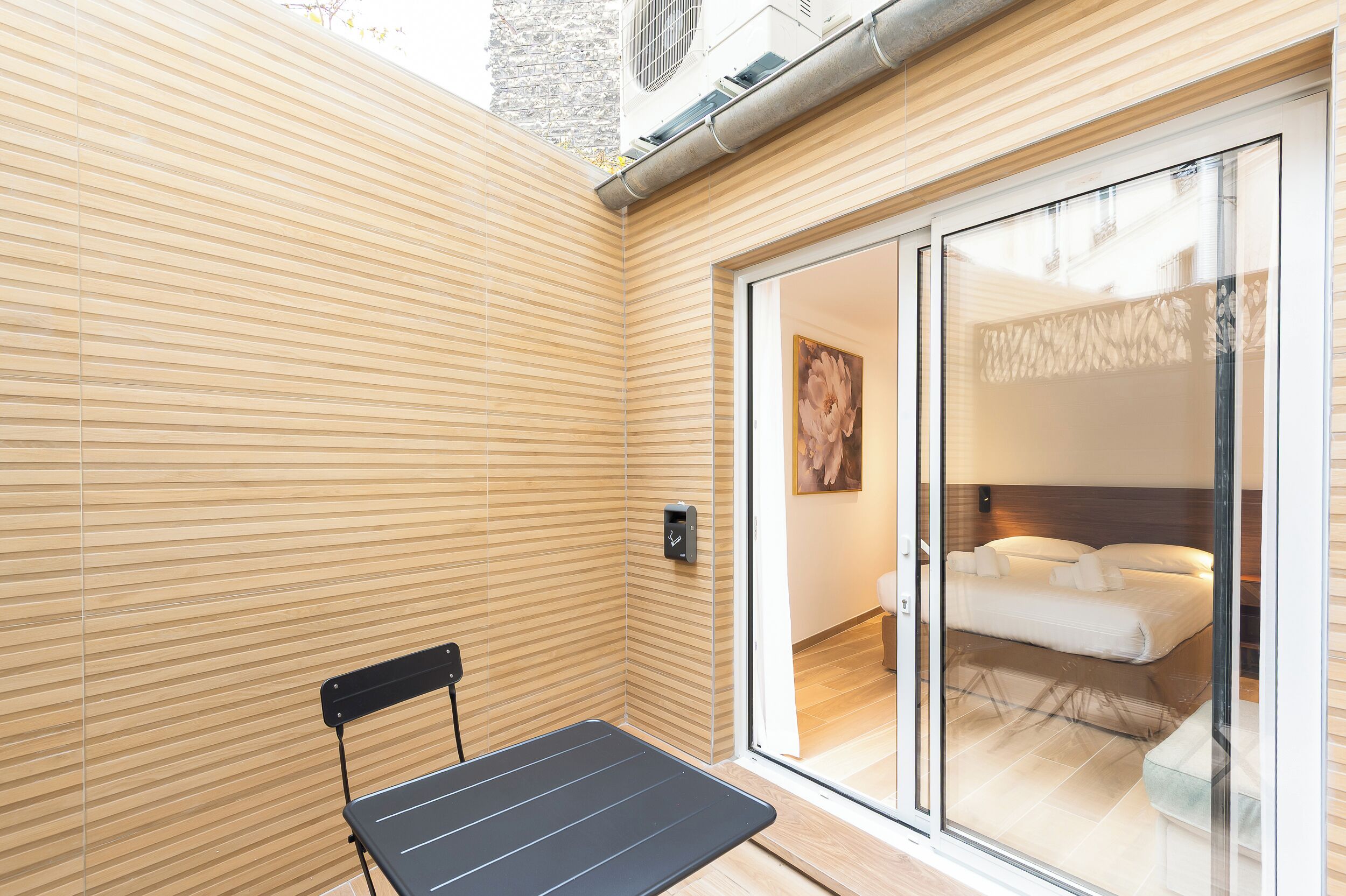 A modern room with a bed, a bench, and a sliding glass door leading to a balcony.
