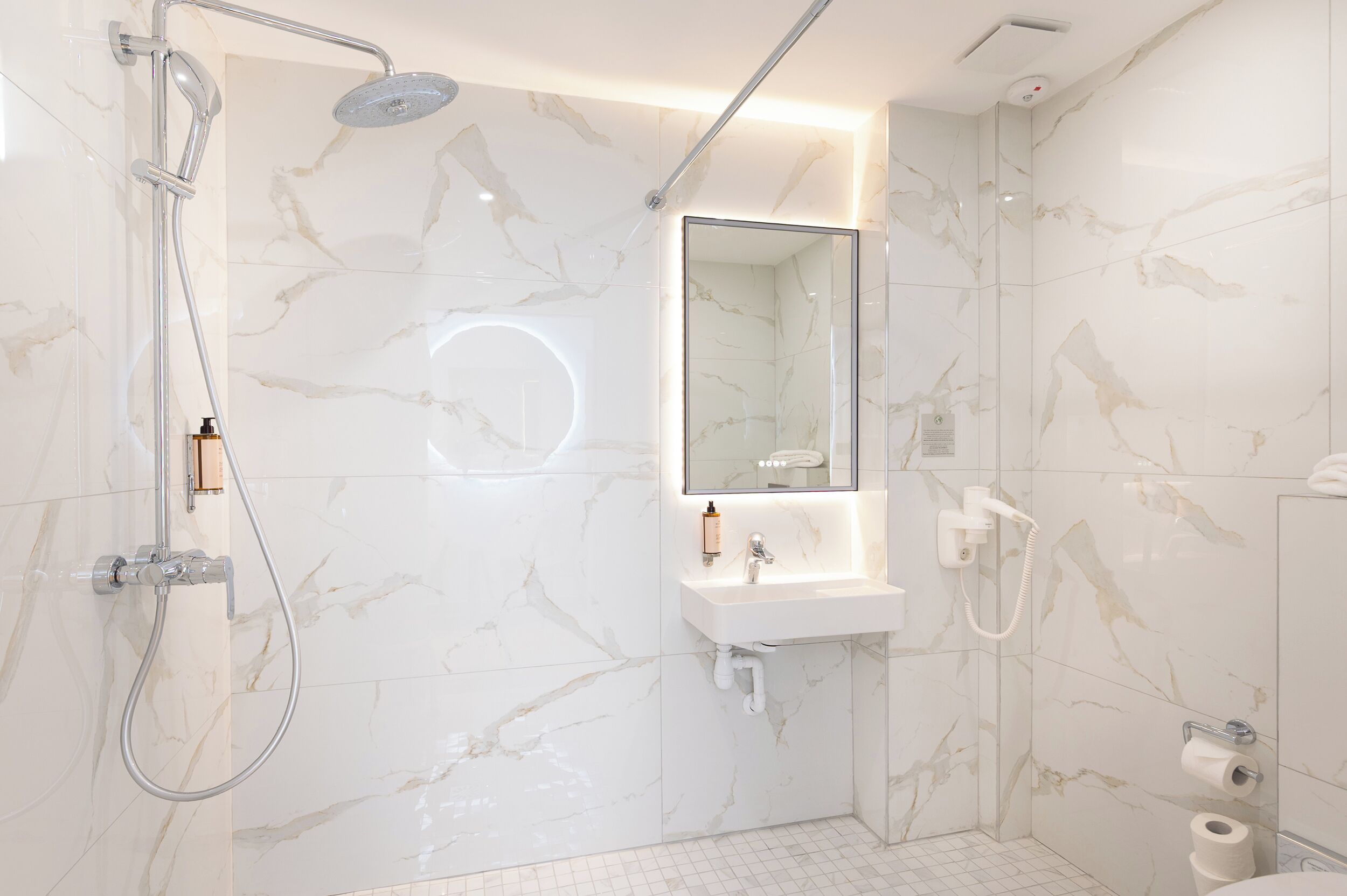 Une salle de bain moderne avec un mur en marbre, un lavabo encastré, un miroir, une douche et des toilettes.