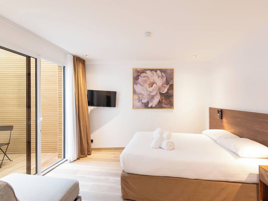 A hotel room with a bed, a flat-screen TV, a painting, and a sliding glass door.