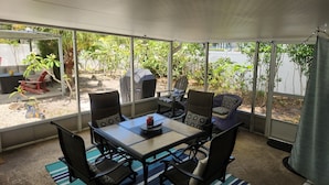 A covered patio area with a table and chairs, a grill, and a view of the garden.