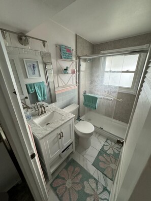 Un baño pequeño con ducha, inodoro y lavamanos.