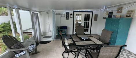A covered patio area with a table and chairs, a small seating area with a bench, and a door leading to an outdoor space.