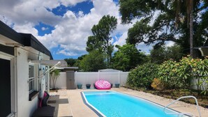 A swimming pool with a white deck, a pink inflatable float, and a covered area with a white fence.