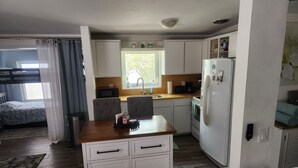 A compact kitchen with a microwave, stove, and refrigerator, a small dining area with a table and chairs, and a bunk bed in the adjacent room.
