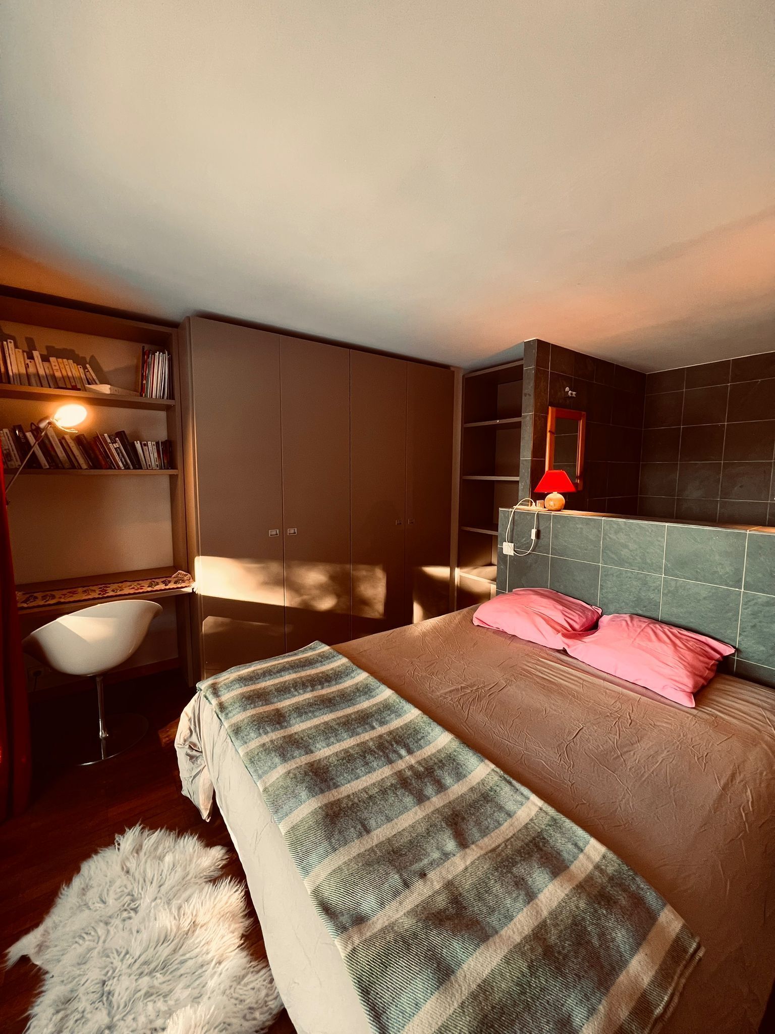Un dormitorio con cama, mesita de noche, silla, estantería y armario.