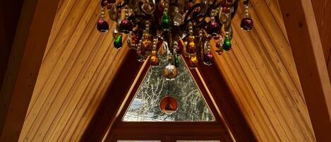 Una habitación acogedora en el ático, con techo inclinado de madera, candelabro, un ventanal con vistas a un paisaje nevado y una mesa de madera con sillas.