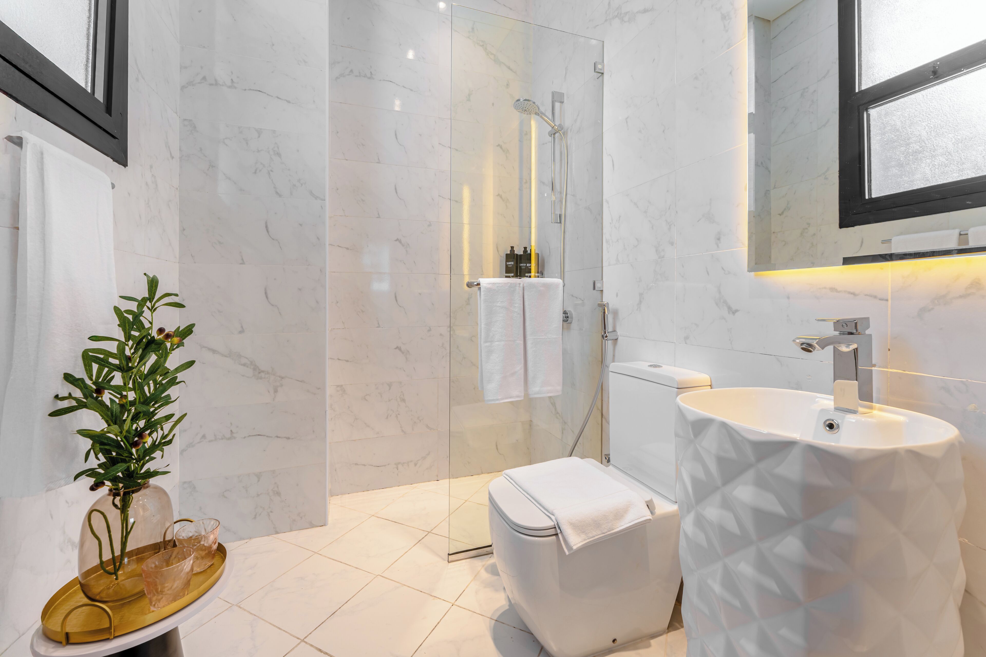 Ein modernes Badezimmer mit einer gläsernen Duschkabine, einer weißen Toilette, einem Standwaschbecken und einem Blumentopf.